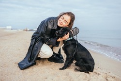 Happy pet owner young woman hugging her dog while sitting on sandy sea shore