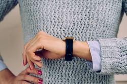 Woman in a gray sweater checks the time on a wrist watch close-up.