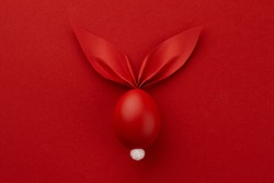 Red Easter egg with paper bunny ears on red background, holiday concept