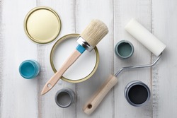 Paint brush, sponge roller, paints, waxes and other painting or decorating supplies on white wooden planks, top view