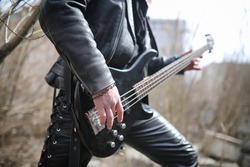 Rock guitarist on the steps. A musician with a bass guitar in a leather suit. Metalist with a guitar on the background of industrial step.