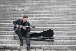 Rock guitarist on the steps. A musician with a bass guitar in a leather suit. Metalist with a guitar on the background of industrial step.