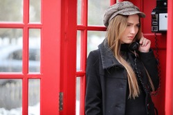 Beautiful young girl in a phone booth. The girl is talking on the phone from the payphone. English telephone booth in the street and a woman talking on the phone.