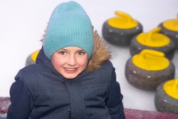 
portrait of a european boy in winter clothes on a background of ice with curling equipment