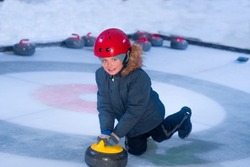 boy on ice plays curling sport game. child pushing a sports equipment stone