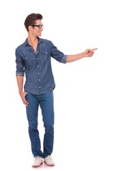 casual young man standing with a thumb in his pocket and pointing and looking to his side with a smile on his face. isolated on a white background