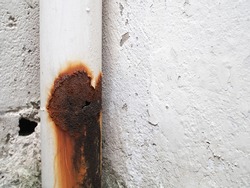 rusted and leaking white aluminium water pipe, damage hole with water flow trace on joint of sewer pipe on concrete wall outside residential, closeup with copy space