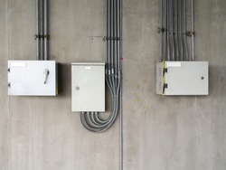 three aluminum electricity system control box with steel electric conduit pipes Installed on gray concrete wall, factory lighting control panel