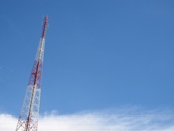 single communication transmitter tower with wireless antennas and wires, red and white steel framework of telecommunication tower with clear blue sky and cloud with copy space