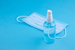 Alcohol gel hand sanitizer and disposable hygienic mask on blue background with copy space. Bottle of hand sanitizer, antimicrobial liquid spray, germ prevention or antibacterial hygiene, copy space.