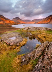Scenic view of mountains and lake at sunset with golden light and moody clouds. Wastwater, Lake District, UK.