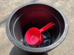a red plastic water dipper in a black tub filled with a little water