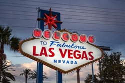 Dusk view of the famous Welcome to Fabulous Las Vegas sign with palm trees and overhead wire grid in background.