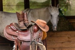 Western riding scenery: A western saddle, western boots and a cowboy hat with a horse in the background