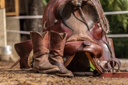 Ranch life scenery: Muddy western boots and a cowboy hat in front of a western saddle. Western riding concept