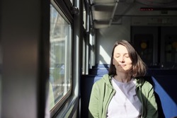 Peaceful caucasian woman with closed eyes enjoying being alone in the train. Mental health concept. Beautiful shadows from sunlight.