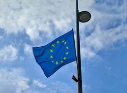European Union flag standing on a street light pole and fluttering in the wind. Dramatic cloudy sky in the background