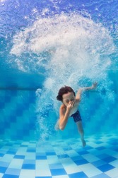Funny portrait of boy swimming and diving in blue pool with fun - jumping deep down underwater with splashes and foam. Family lifestyle and summer children water sports activity with parents.