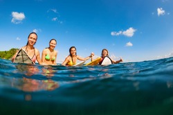 Happy girls in bikini have fun - group of surfers sit on surf boards, young women wait for big ocean wave. People in water sport adventure camp, beach extreme activity on summer beach family vacation.