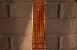 Acoustic guitar fingerboard closeup on white brick wall background. Fret of guitar on neutral background.
