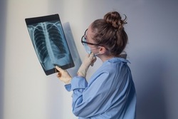 Doctor is looking at xray of lungs and thinking. Female lung specialist in glasses examining MRI or computer tomography picture. Covid diagnostics concept. Work of radiologist.