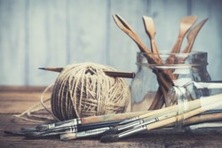 
Art and craft tools. Artist's brushes, sculpturing set and pencil in glass jars on rustic background. Selective focus.