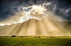 The rays of the sun from behind the clouds illuminate the valley. Sunrays from sky clouds. Cloudy sky sunrays. Beautiful sunrays from cloudy sky
