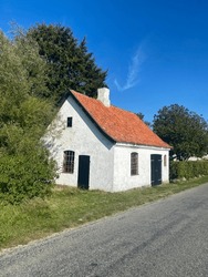 White house with orange roof at the side of road around by trees and blue sky at the background at denmark countryside