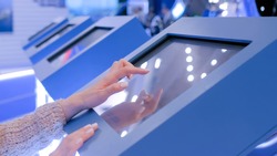 Education and technology concept - woman using interactive touchscreen display of electronic kiosk at technology exhibition