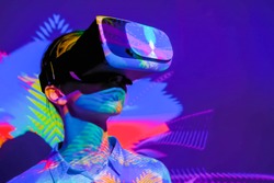 Woman using virtual reality headset, looking around at interactive technology exhibition with multicolor projector light illumination. VR, augmented reality, immersive, entertainment concept