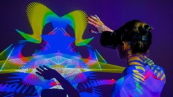 Woman using VR headset and waving hands in front of large wall display with augmented reality mirror effect at modern futuristic immersive exhibition or museum. AR, future, art, technology concept
