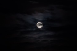 Bright white full moon rising against black dark sky at night with clouds. peaceful, astronomy, mystical, halloween, moonrise and nature concept