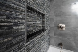 Renovated modern bathroom with bathtub. Dark (Black Grey) tiles accent wall and niche with Grey tiles and white bathtub. 