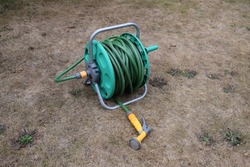 Garden hose reel sitting unused on a dry lawn. Hosepipe ban in UK due to drought.
