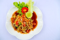 Somtum, traditional Thai food Papaya, tomatoes, green beans and peanuts garnish with lime salad in a white plate, top view.