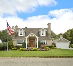 American Flag Beautiful Suburban Brick Cape Cod style home blue sky clouds USA