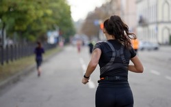 Woman with ponytail running marathon on empty city road, sweat on her black sportswear, other runners on blurred background. Active female taking part in sports event