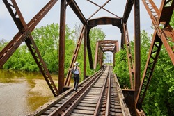 People walking on railroad tracks across bridge with river flowing underneath