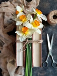 Bouquet of daffodil flowers on the books tied of twine, skein of twine, old scissors and airy fabric on black concrete background. Flatlay with spring flowers and selective focus. Narcissus.