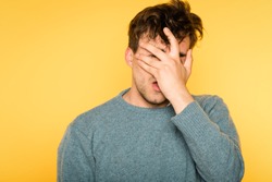 facepalm. desperate frustrated man covering his face. hopeless situation and regret or hangover. portrait of a young brunet guy on yellow background. emotion facial expression and feelings concept.