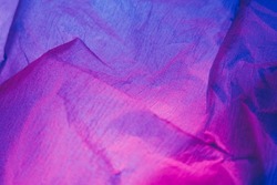 Creased paper texture. Ultraviolet background. Crushed material. Neon iridescent pink purple blue color gradient light grain noise wrinkled abstract surface.