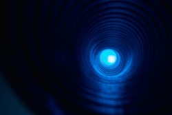Defocused neon glow. Futuristic background. Fantasy tunnel. Blur fluorescent blue color round spotlight in ripple whirl texture pipe on dark black empty space.