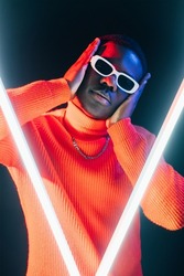 Modern fashion. Vogue dance. Neon light night. Cool serious stylish man studio portrait in sunglasses bright orange LED glow on dark background.