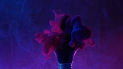 Neon smoke background. Paint water mix. Creative idea. Blue pink color ink splash in broken light bulb on purple floating mist abstract art texture.