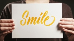 Smile sign. Positive motivation. Encouraging message. Unrecognizable woman supporting with optimistic support word text placard in hands.