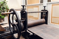 Old printing press in museum, historical exhibition. Close-up of ancient paper printing machine, printery exponent. Gallery with showpieces on background