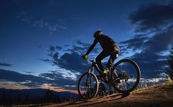 Cyclist sitting on bicycle under cloudy night sky.