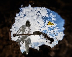 View from inside fossil pit of person in white jumpsuit and gas mask, standing outdoors near totenkopf sign and burying hazardous substances in the ground for disposal.