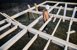 Man worker building wooden frame house on pile foundation. Carpenter installing wooden truss for timber framing. Carpentry concept.