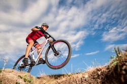 Low, wide angle portrait against blue sky of mountain biker going downhill. Cyclist in red sport equipment and helmet
